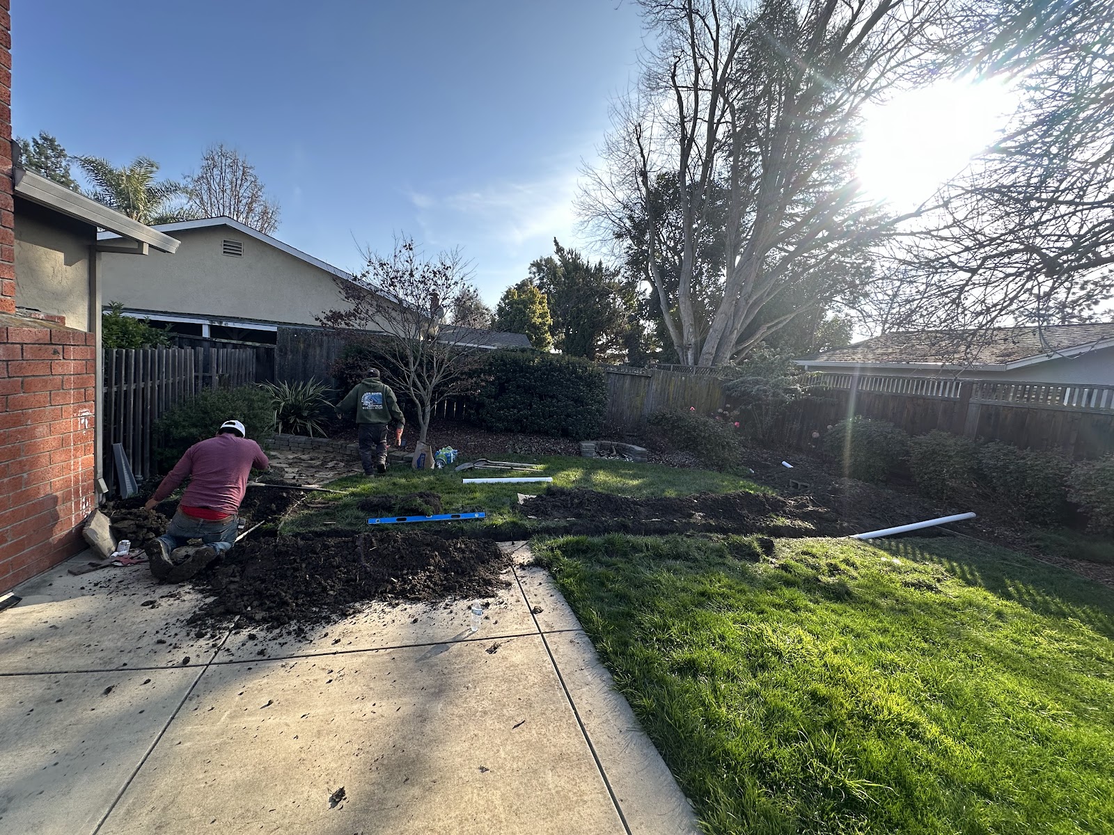 Crew trenching beside the old concrete slab with pipe laid on the lawn