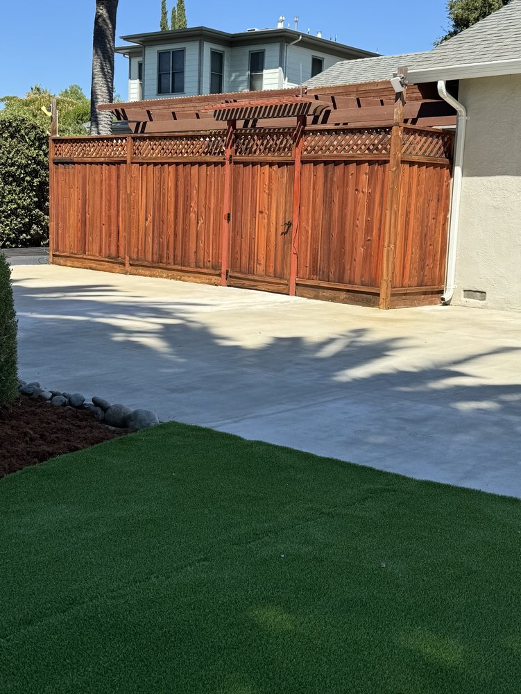 Redwood screen fence with lattice top and a pergola-style cap, standing where the concrete meets the turf lawn