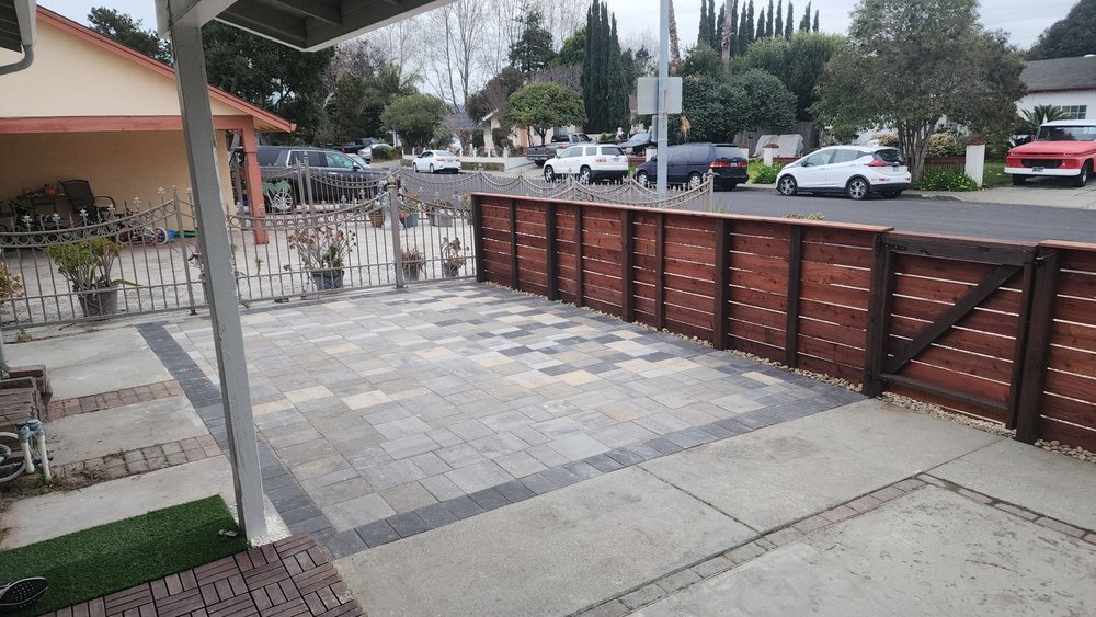 Paver patio with a dark border behind the horizontal redwood fence and gate at the Fremont home