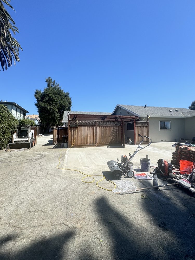 Milpitas property during demolition: the old cracked driveway broken up, with a skid steer, mixer and tools on site in front of the house