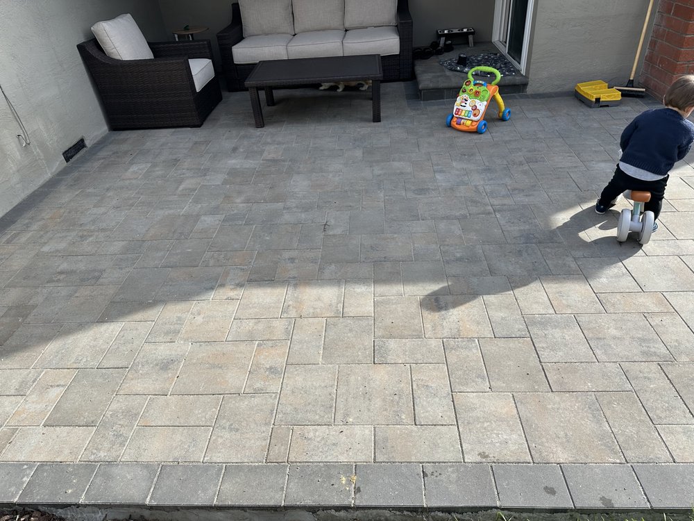 Finished stone paver patio in Fremont with outdoor furniture against the house and a darker paver border along the front edge