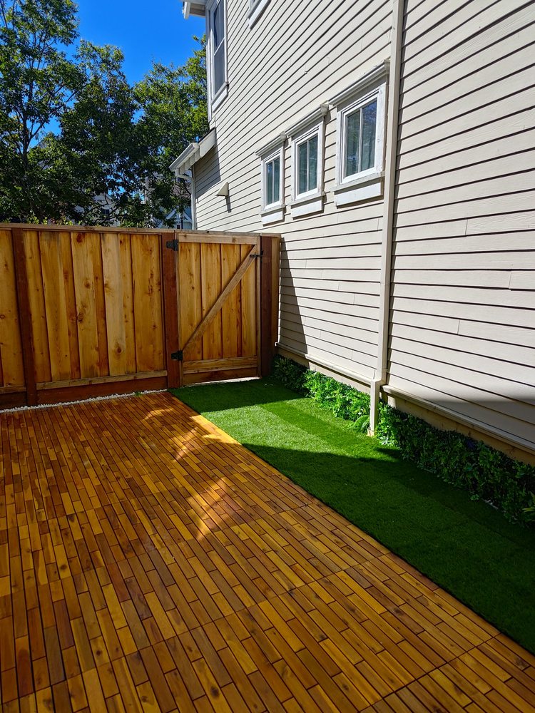 Wood fence and gate with artificial turf and wood deck tiles in a sunny side yard