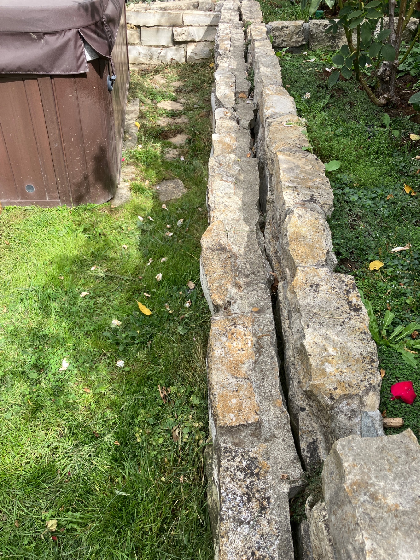 Before restoration: cracked, leaning vintage stone retaining wall beside the rose beds and hot tub at Georgeta’s Lafayette property