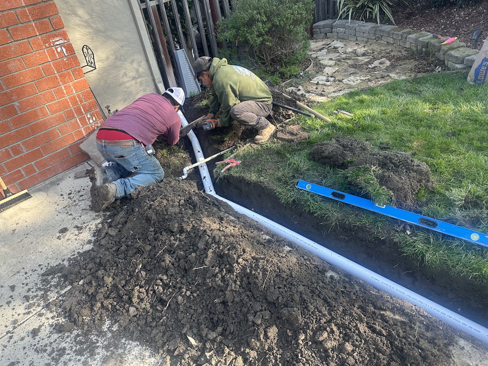 Two crew members setting pipe in a trench along the house next to the old slab