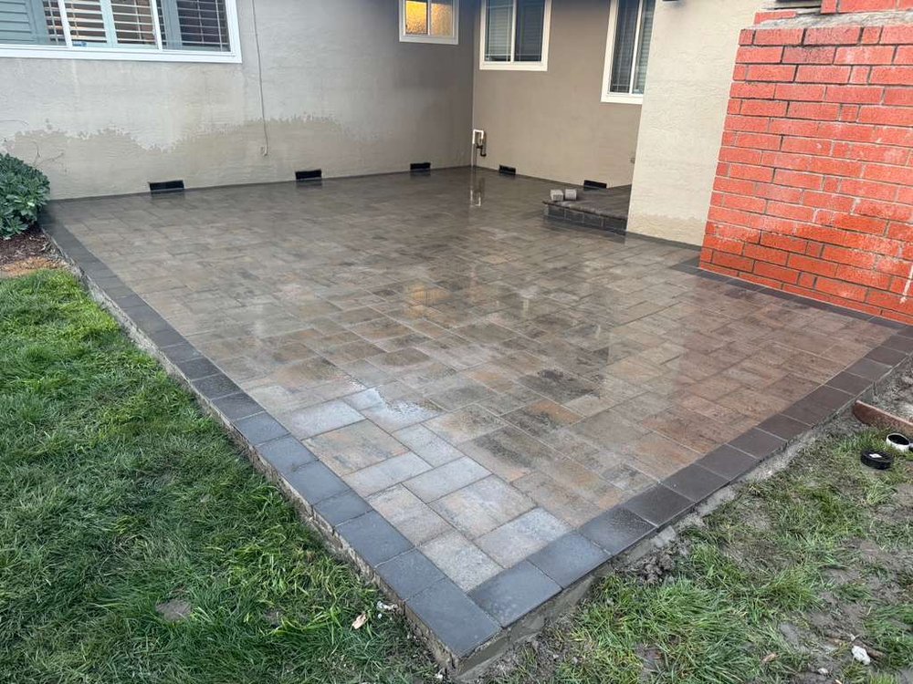 Freshly laid, wet paver patio behind a Fremont house with a dark border and the new step at the slider
